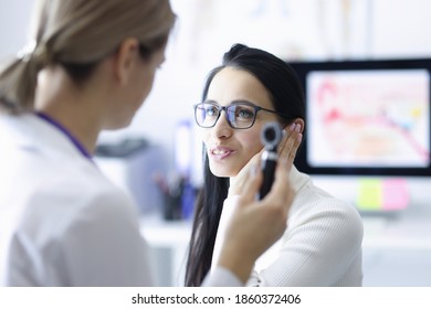 Woman patient holding ear near doctor with otoscope in hand in clinic. Diagnosis and treatment of hearing loss concept
