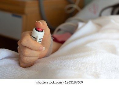Woman patient  in hospital dress under white blanket holding red emergency call button while lying in  bed.Hand holding  nurse call button,selective focused.