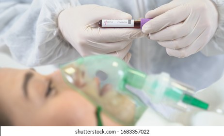 A woman patient is receiving ventilation, oxygen because she's infected by coronavirus. A doctor is showing positive  test tube in background.	
