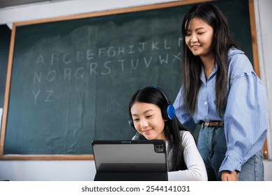 A woman patiently helps a young girl using a tablet. The girl, wearing headphones, is focused on the screen, while the woman smiles warmly, creating a supportive and encouraging learning environment - Powered by Shutterstock