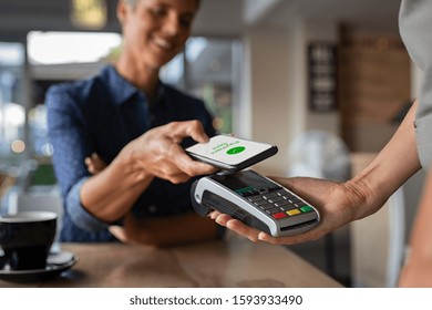 Woman paying bill through smartphone using NFC technology in a restaurant. Satisfied customer paying through mobile phone using contactless technology. Closeup hands of mobile payment at a coffee shop
