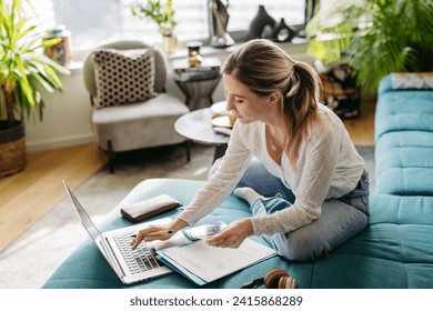 Woman paying bills online, sitting in living room, working on notebook. Online banking, internetbanking at home throught website, app. - Powered by Shutterstock