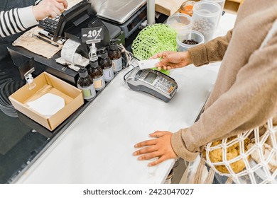 Woman paying with contactless credit card in local zero waste grocery store at cash desk - Powered by Shutterstock