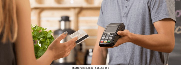 Woman Paying With A Debit Card In A Restaurant, Waitress Holding A Payment Terminal