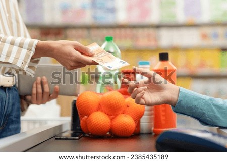 Woman paying for her groceries at the supermarket checkout, she is giving cash money to the cashier