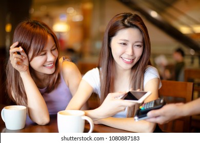 Woman Paying With Mobile Phone In Cafe Shop