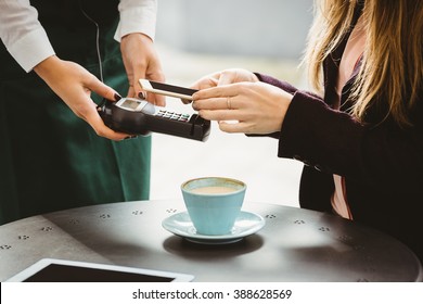 Woman Paying With Mobile Phone In Cafe