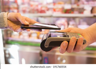 Woman Paying With NFC Technology On Mobile Phone, In Supermarket 