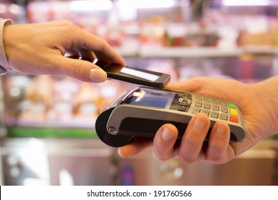 Woman Paying With NFC Technology On Mobile Phone, In Supermarket 