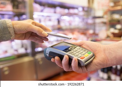 Woman Paying With NFC Technology On Mobile Phone, In Supermarket 