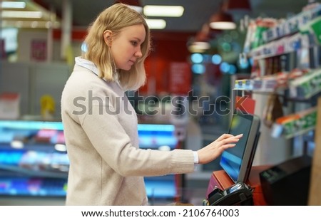 Woman pays at self-checkouts in supermarket.
