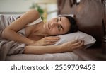 A woman peacefully sleeping on a soft pillow, wrapped in a cozy blanket, in a stylish bedroom with a wooden headboard and natural light. Relaxation, comfort, and restful sleep atmosphere.