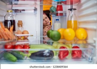Woman peeking in the fridge full of groceries. Unhealthy eating concept. Picture taken from the inside of fridge. - Shutterstock ID 1238409364