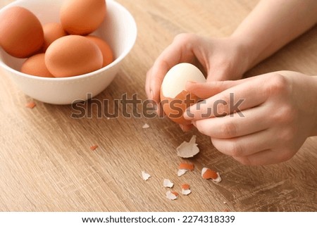 Woman peeling boiled egg on wooden table, closeup