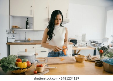 A woman peeling a carrot in a bright, modern kitchen with fresh vegetables and wooden countertops, showcasing healthy cooking. - Powered by Shutterstock