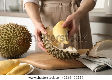 Woman peeling durian at table in kitchen, closeup