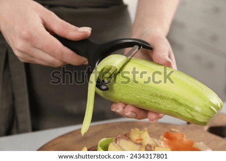 Woman peeling fresh zucchini at table indoors, closeup