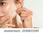 Woman peeling off face mask on light grey background, closeup