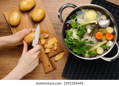 Woman peeling potato for cooking tasty bouillon at wooden table, top view - Powered by Shutterstock