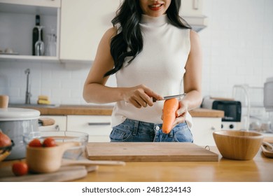 A woman peels a carrot in a modern kitchen, surrounded by fresh vegetables and kitchen utensils, promoting healthy home cooking. - Powered by Shutterstock