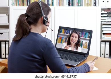 Woman with pen and paper and a headset in front of her laptop making a video call with her friendly tutor, e-learning concept