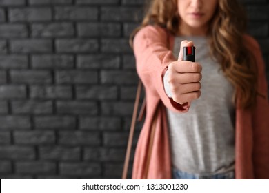 Woman with pepper spray for self-defence against dark brick wall