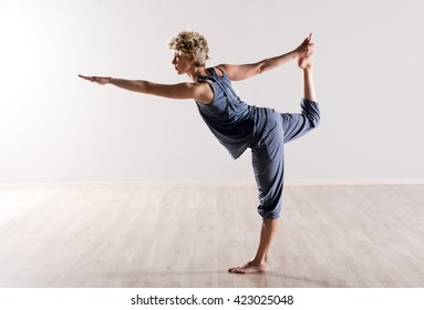 Woman in perfect balance while holding foot during intense yoga practice in studio with bright background and hardwood floor