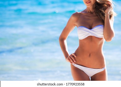 Woman with perfect body in white bikini posing on sea background