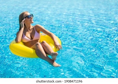 Woman With Perfect Sexy Body In Bikini And Glamorous Sunglasses, Posing On An Inflatable Yellow Ring In The Swimming Pool Outdoors