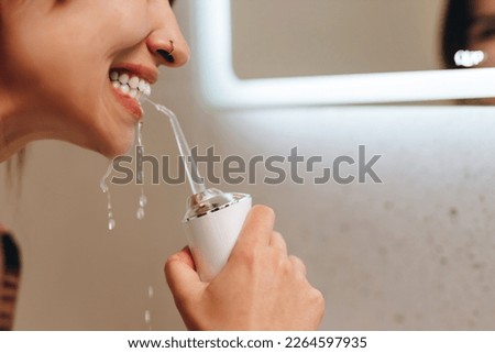 Woman with perfect white smile using portable water flosser or oral irrigator.