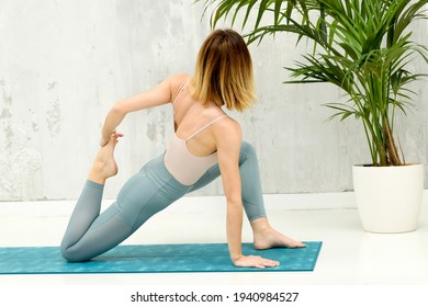 Woman Performing A Low Lunge Variation Yoga Pose In A Low Angle Rear View As She Twists To Hold Her Foot To Strengthen And Stretch Her Quads, Hip Flexors And Groin In A Rear View