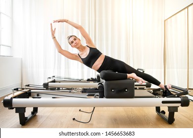 Woman performing a pilates yoga mermaid exercise or side stretch to tone the intercostal muscles on a reformer bed in a gym - Powered by Shutterstock