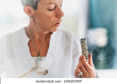 Woman performing ritual of sage burning to cleanse space from negative energy. Physical, mental, and emotional well-being.