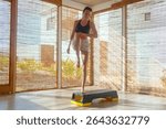 A woman performs an exercise routine on a step platform in a bright indoor space, surrounded by scenic outdoor views.