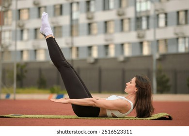 A woman performs a Pilates leg raise on a yoga mat in an urban outdoor setting, focusing on core strength and control. This image captures the balance between fitness and mindfulness in modern health - Powered by Shutterstock