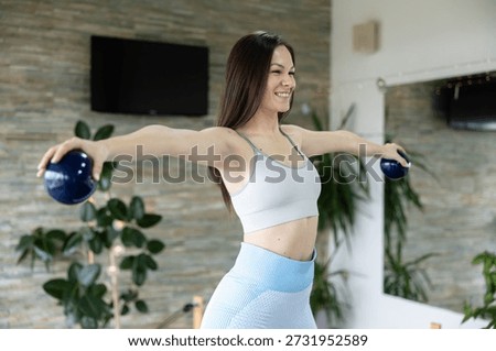 The woman performs a Pilates session, emphasizing balance and core stability with weights in hand.