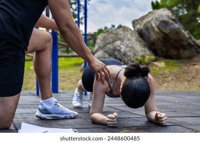 A woman performs a plank as a trainer guides her posture during an outdoor workout session. - Powered by Shutterstock