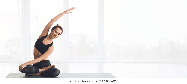 A woman performs a side stretch in a modern yoga studio filled with natural light, panorama with copy space - Powered by Shutterstock