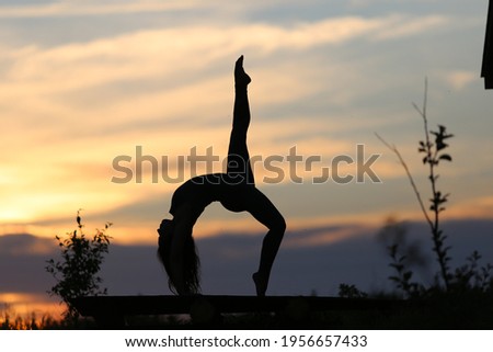 A woman performs vigorous yoga at sunset. Orange sky, natural landscape