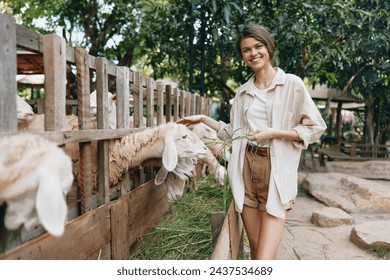 A woman is petting a goat behind a fence in a zoo or farm
