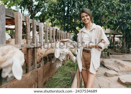 A woman is petting a goat behind a fence in a zoo or farm