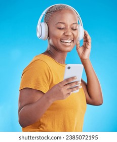 Woman, phone and headphones for music, listening to audio and social media influencer on a blue background. Young african person on mobile, video streaming subscribe and radio or selfie in studio