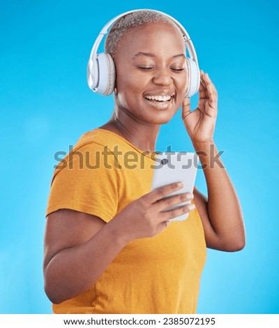 Woman, phone and headphones for music, listening to audio and social media influencer on a blue background. Young african person on mobile, video streaming subscribe and radio or selfie in studio