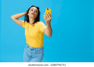 Woman with a phone in her hands with a yellow case on a blue background in a yellow T-shirt, emotions signals gestures, online lifestyle concept, shopping, communication, learning, business online - Shutterstock ID 2280796711