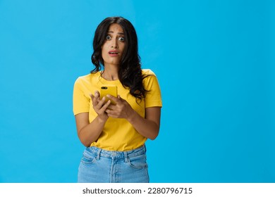 Woman with a phone in her hands with a yellow case on a blue background in a yellow T-shirt, emotions signals gestures, online lifestyle concept, shopping, communication, learning, business online - Shutterstock ID 2280796715