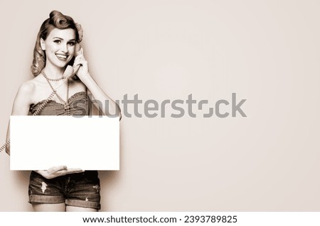 Woman with phone, in pinup cloth, showing blank signboard with mock up copy space free text area. Pin up girl pose in retro fashion vintage studio concept. Brown toned black and white bw photo