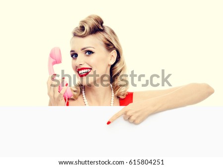 Woman with phone, in pin-up style dress, showing blank signboard with copyspace area. Caucasian blond model posing in retro fashion and vintage concept studio shoot.