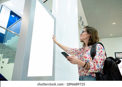 Woman with phone uses self-service desk with touch screen - Shutterstock ID 1896689725