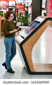 Woman With Phone Uses Self-service Kiosk In The Shopping Mall