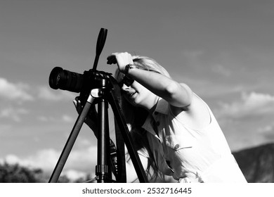 A woman photographer adjusts the camera for shooting. Black and white photo of a beautiful blonde girl with a camera - Powered by Shutterstock